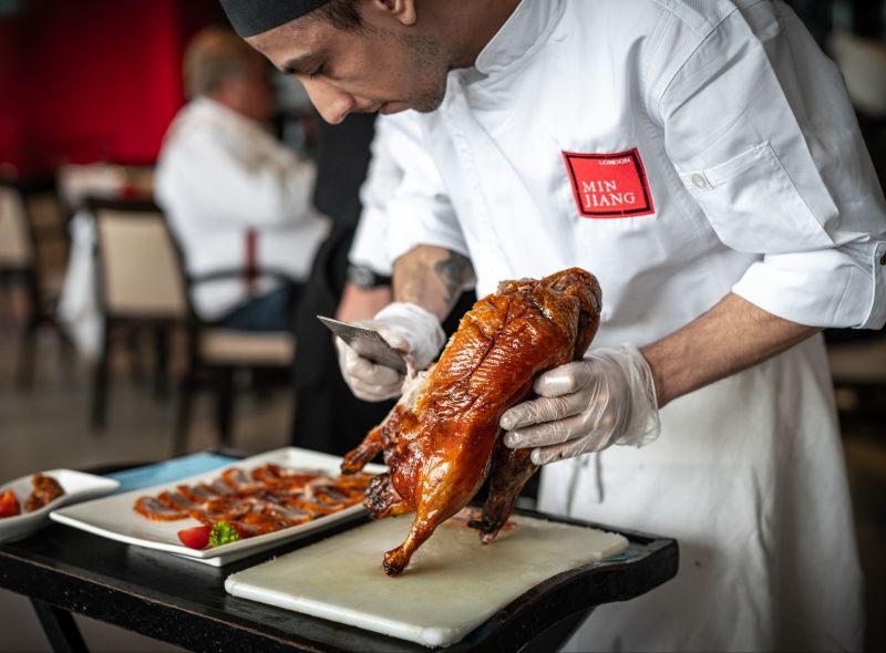 Min Jiang offering signature Wood-Fired Beijing Duck sliced on tableside.